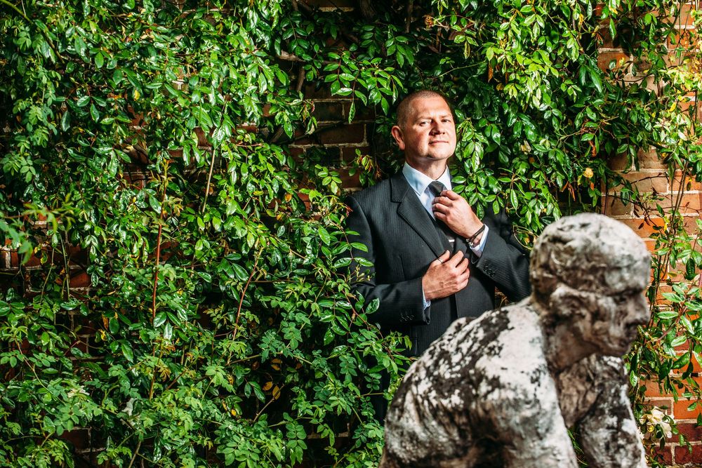A couple shares a joyful moment together outdoors against a lush green garden backdrop and brick wall.