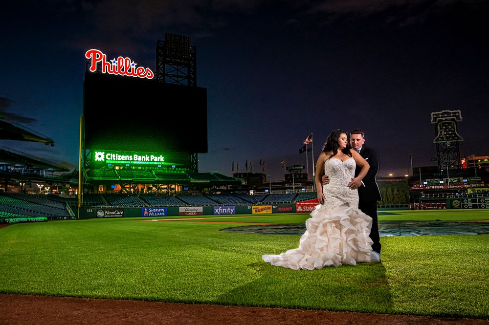 A couple poses for wedding photos on the baseball field at Citizens Bank Park stadium at night.