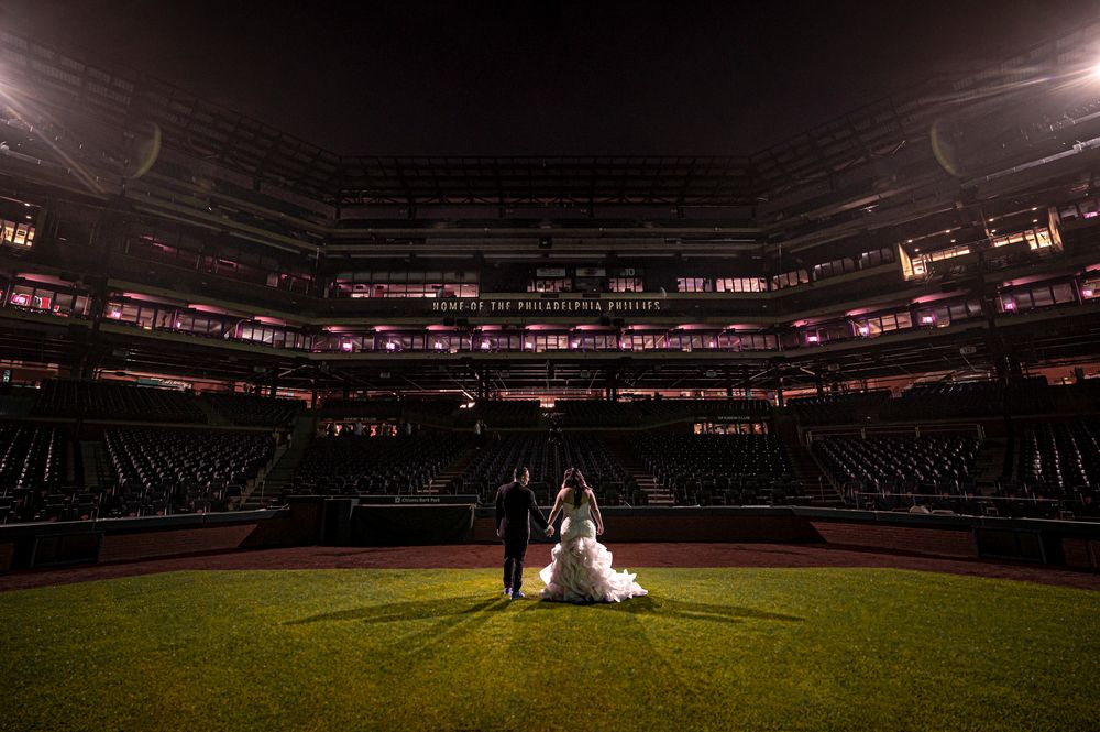 Dramatic nighttime wedding photo on an empty baseball field with stadium lights illuminating the dark stadium interior.