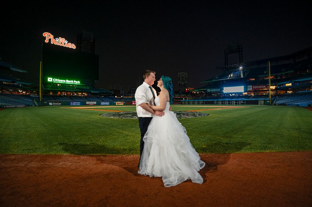 A romantic wedding couple poses on a baseball field at night with stadium lights illuminating the scene.