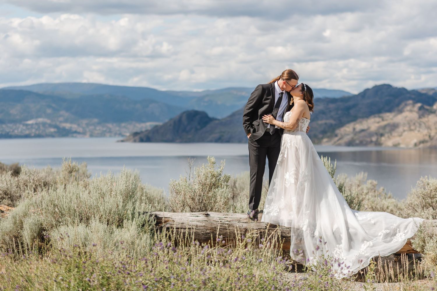 Scenic mountain wedding photos with white dress flowing in breeze against backdrop of lake and sage brush landscape.
