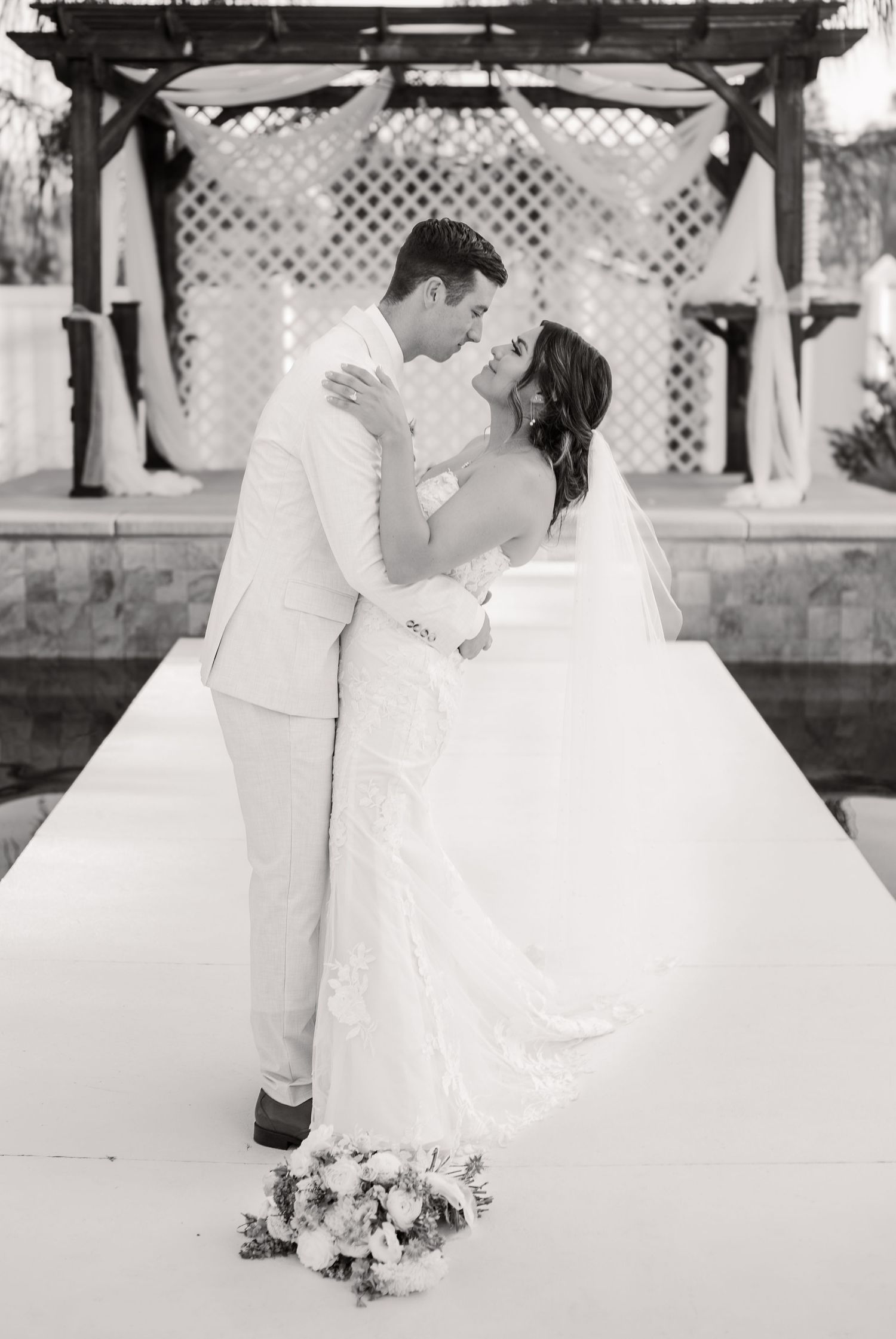 A couple shares their first kiss under a latticed pergola during their black and white wedding ceremony.