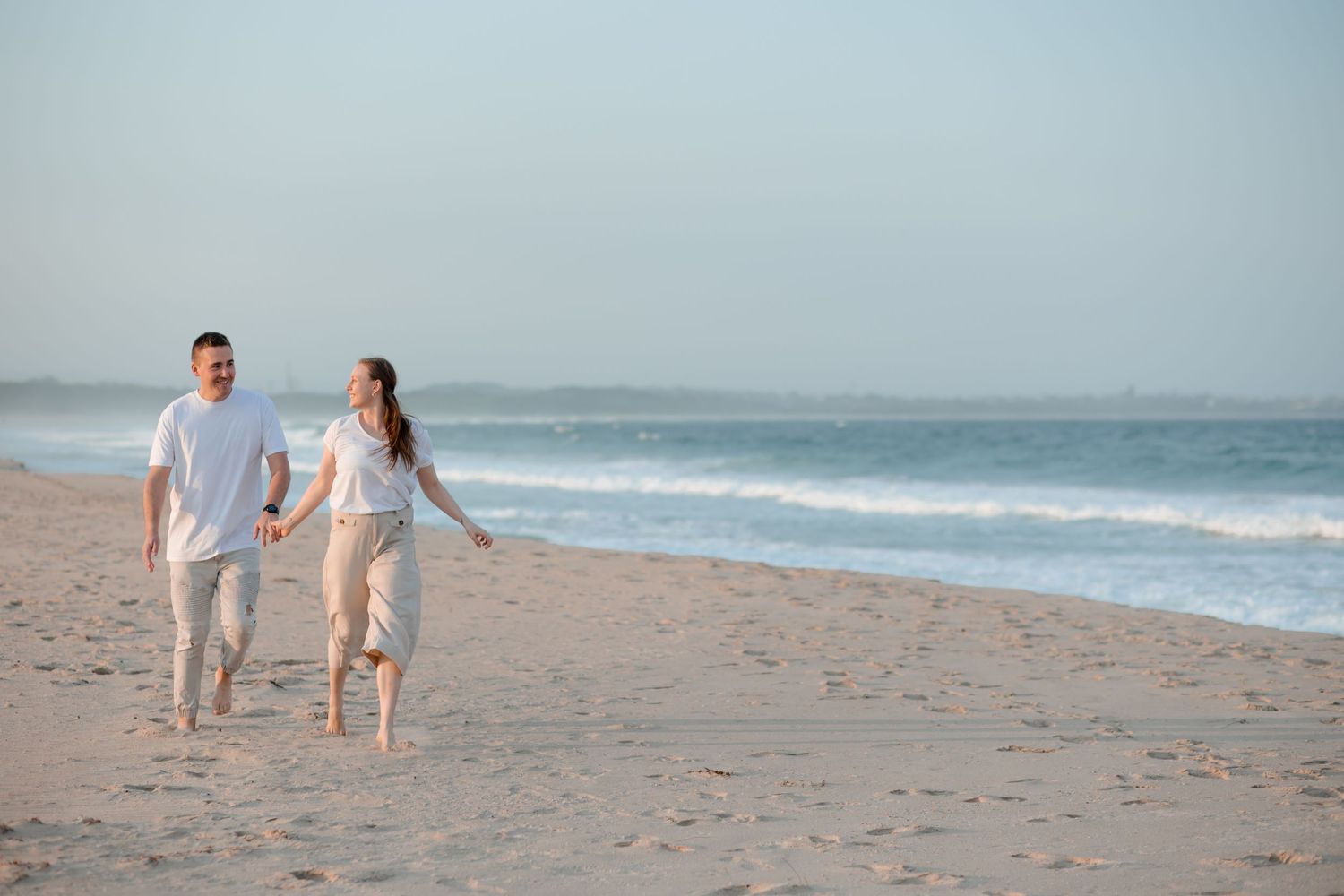 Couple walking along Windang Beach in soft evening light