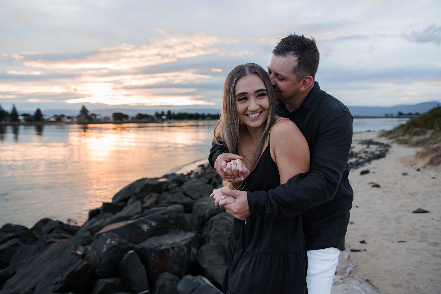 Couple cuddling along Windang Beach in soft evening light. Sunset in the background