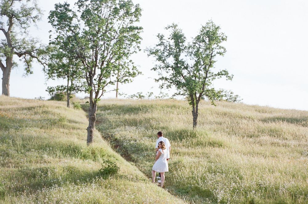 A family walks through a golden grassy hillside with scattered trees during a warm summer evening.