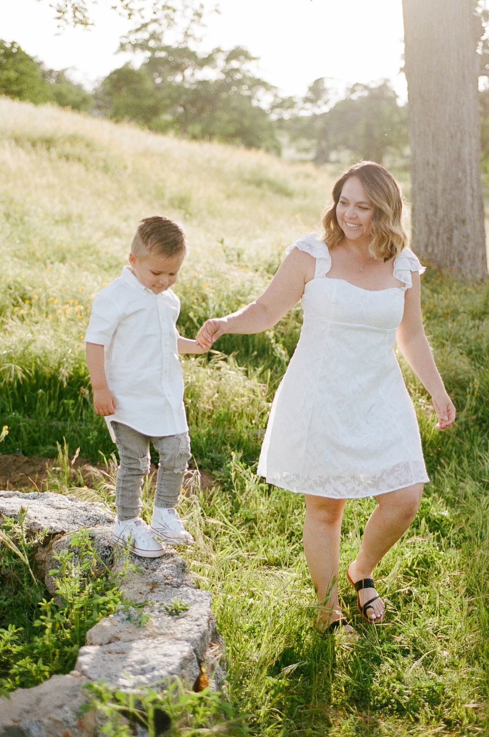 Children in white clothing explore a grassy hillside path during golden hour.