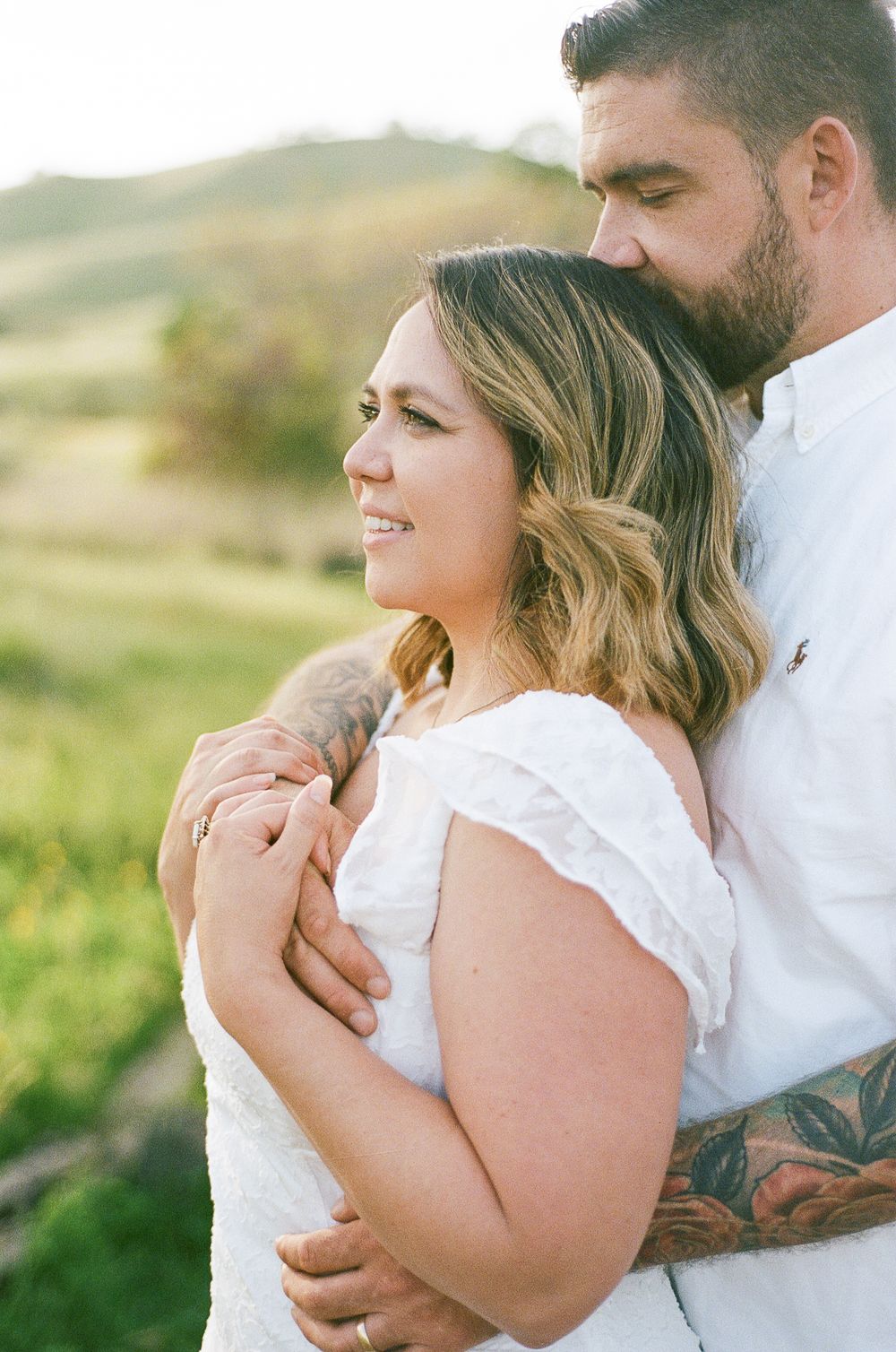 A couple embraces in a romantic outdoor setting with rolling hills and golden sunlight.