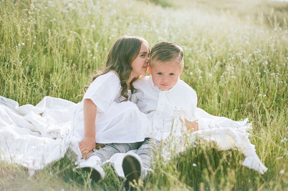 A couple in white clothing shares tender moments together while lying in a sunlit meadow of tall grass.