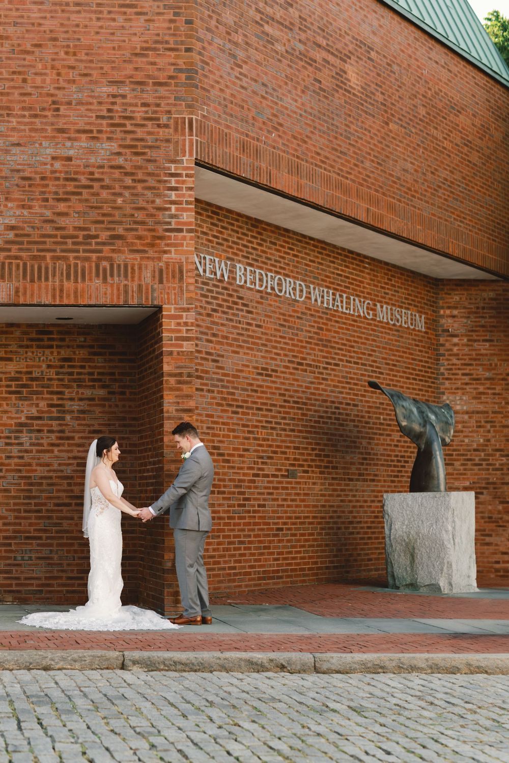 A sequence of three wedding photos taken outside a brick museum building showing playful poses against the wall.