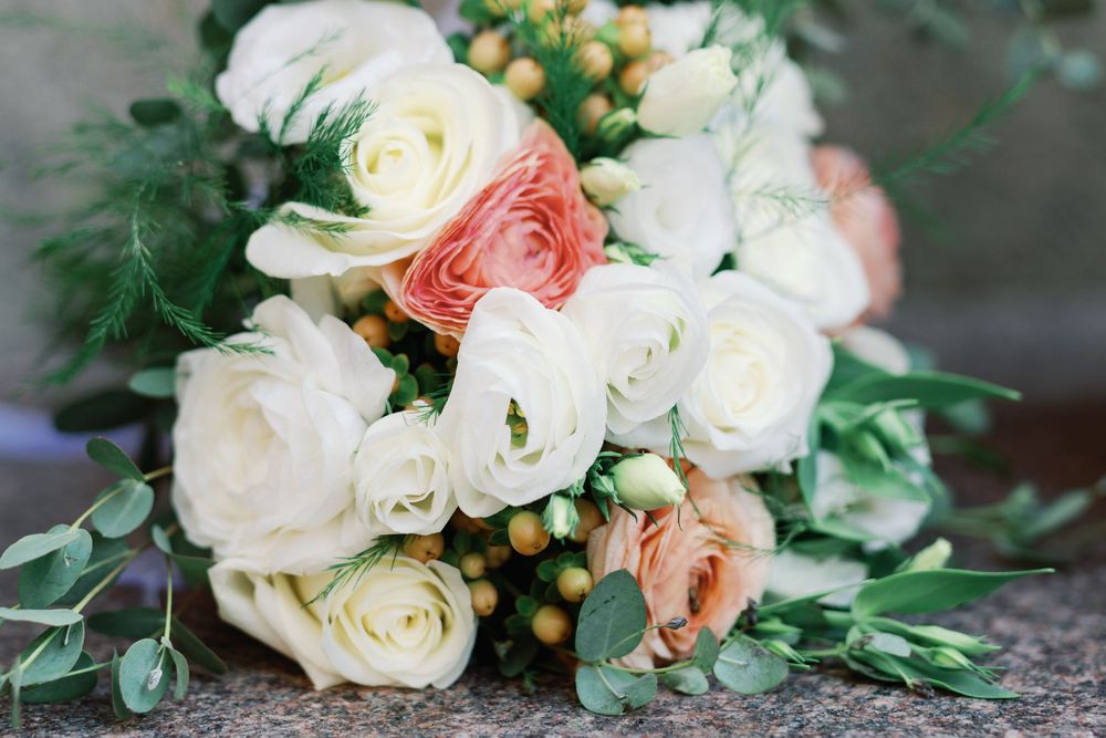 Delicate pink and white roses with orange berries arranged in an elegant wedding bouquet on a stone surface.