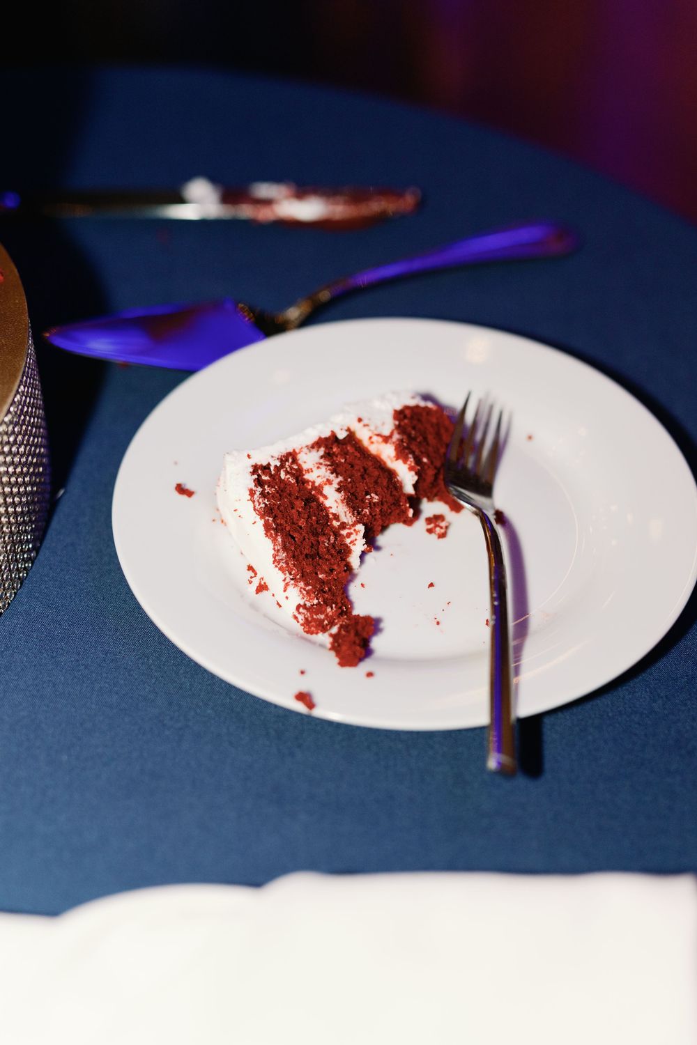 A slice of red velvet cake with crumbs scattered on a white plate against a dark blue tablecloth.