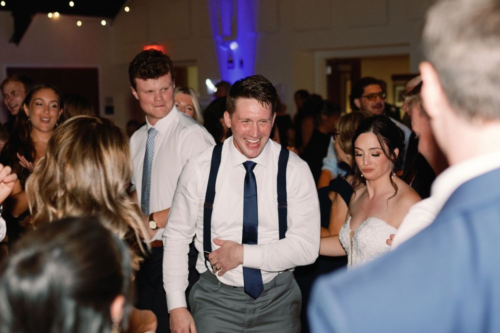 People dancing and celebrating at a wedding reception with blue uplighting and festive atmosphere.