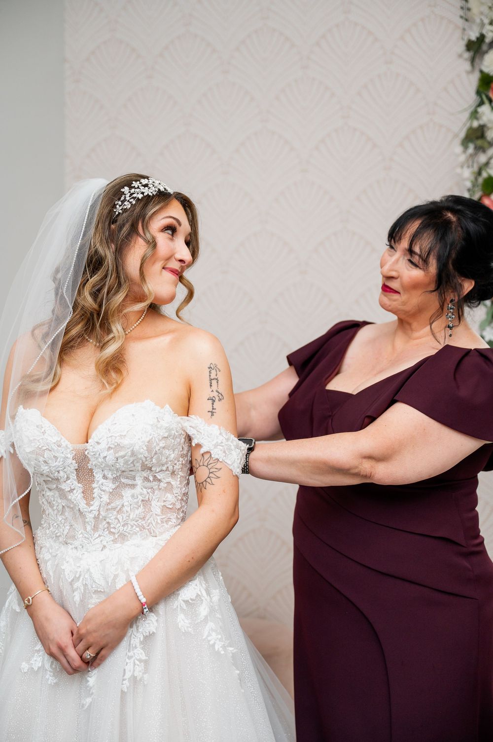 Wedding preparation scene showing bride in white gown with attendant in burgundy dress.