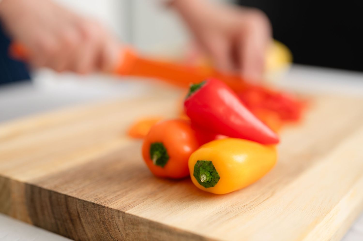 Orange and red bell peppers (food photography) being sliced on a wooden cutting board with a sharp knife at studio in Spring Texas
