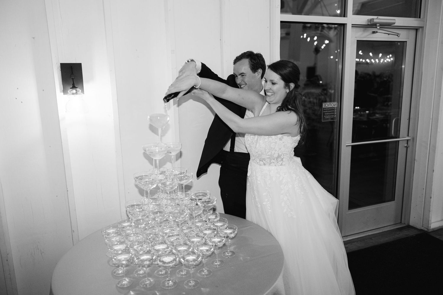 A couple pours champagne into a tower of glasses during an elegant wedding celebration.