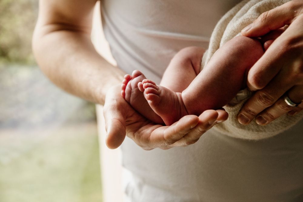 Father gently holding tiny newborn baby feet in his hands outdoors.