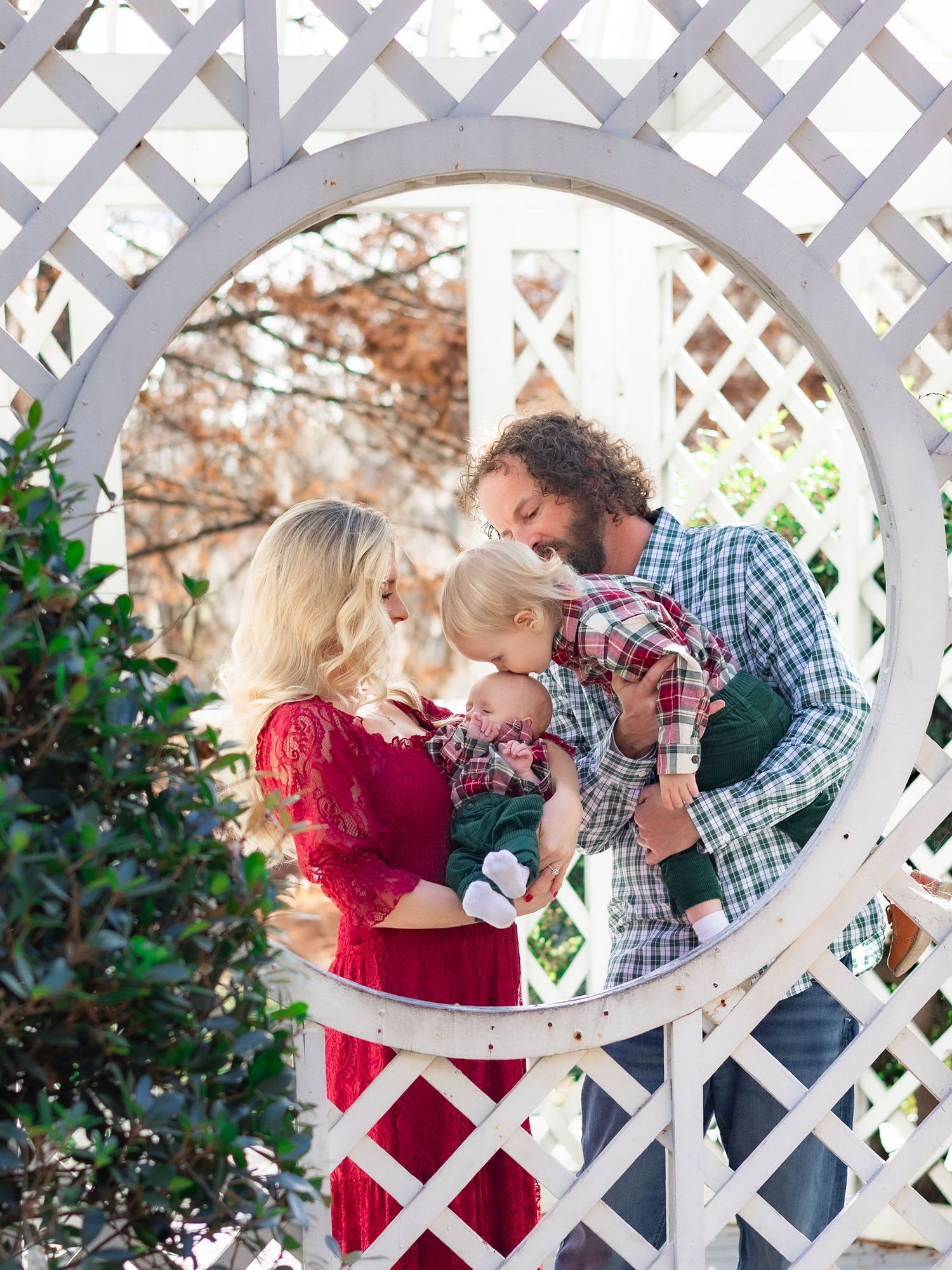 A couple shares a romantic moment through a white lattice garden trellis in an outdoor setting.