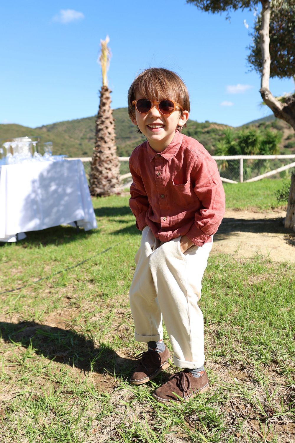 A joyful moment captured outdoors on a grassy hillside with palm trees and mountains in the background.