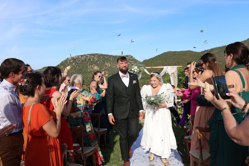 Wedding guests form a receiving line outdoors to celebrate and congratulate the newlyweds on a sunny day.