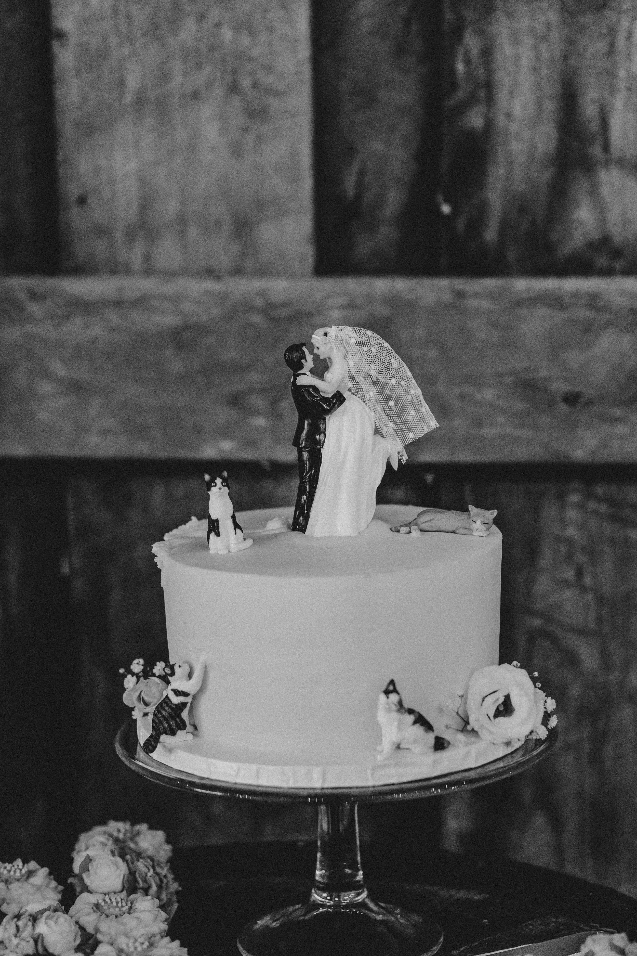 A black and white photo of a wedding cake with miniature figures on top and around the sides.