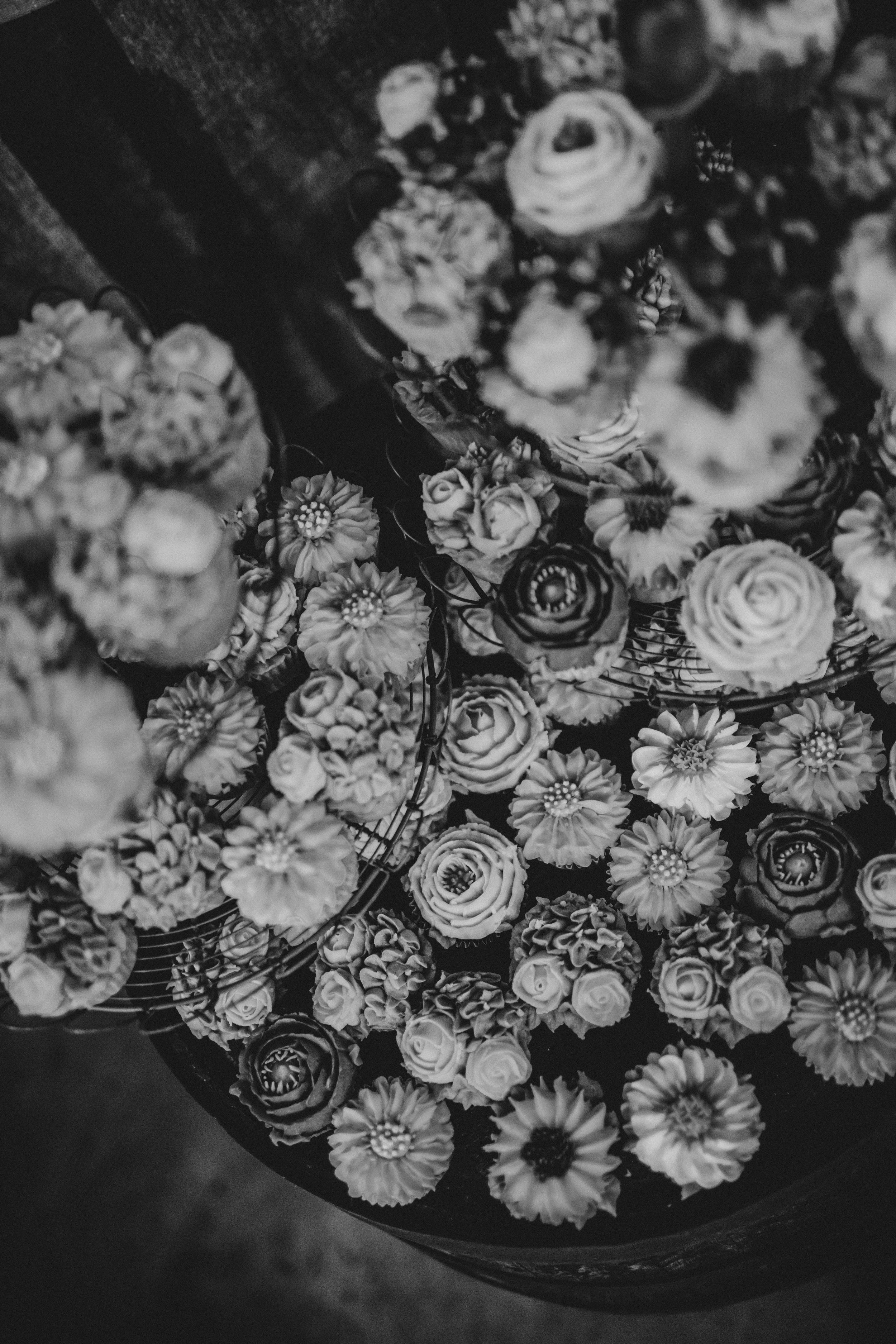 A black and white photograph of a bouquet of various flowers in a round container, showcasing roses and daisies.