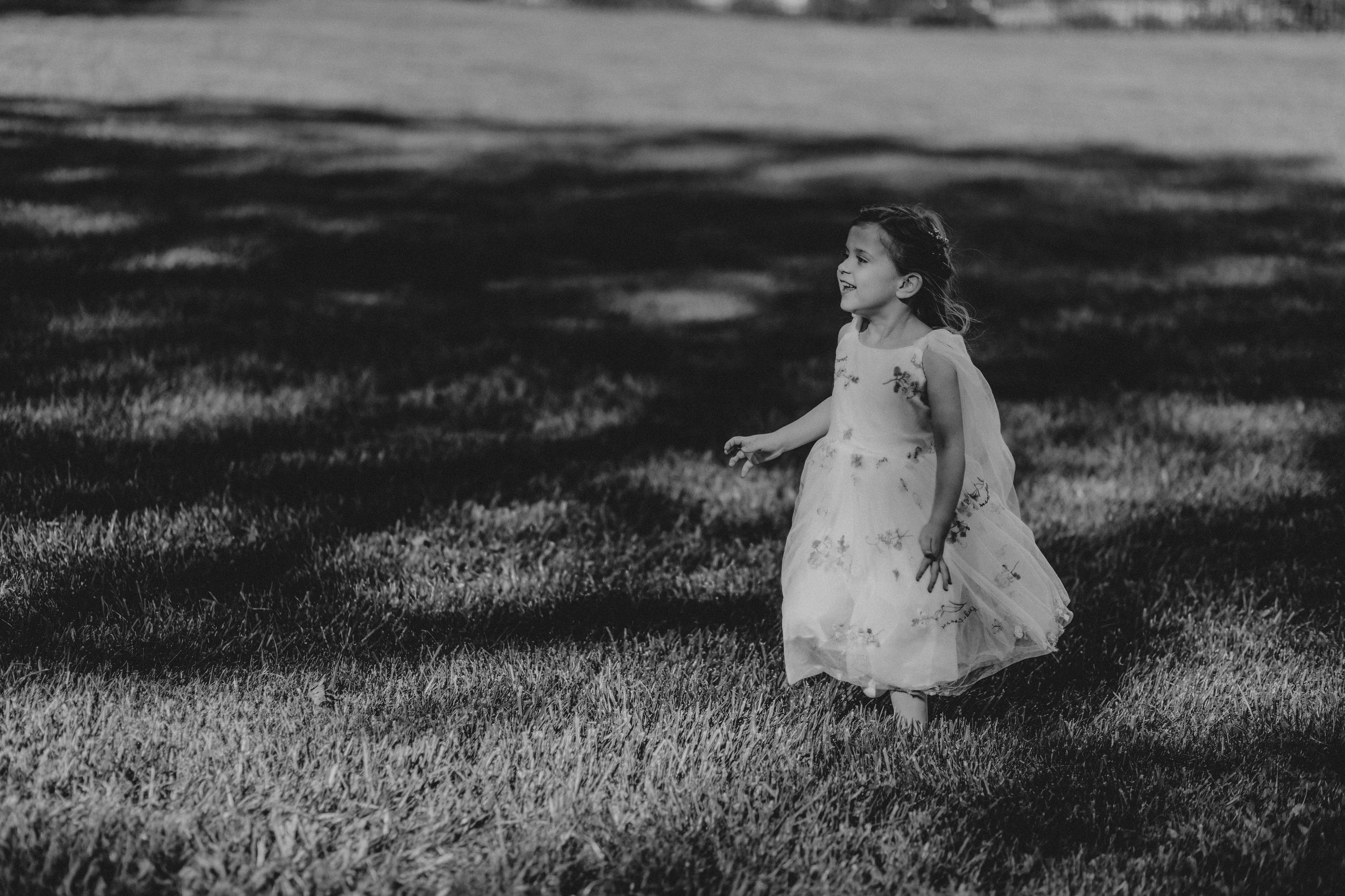 Young girl in white dress walking on grass in dappled sunlight.
