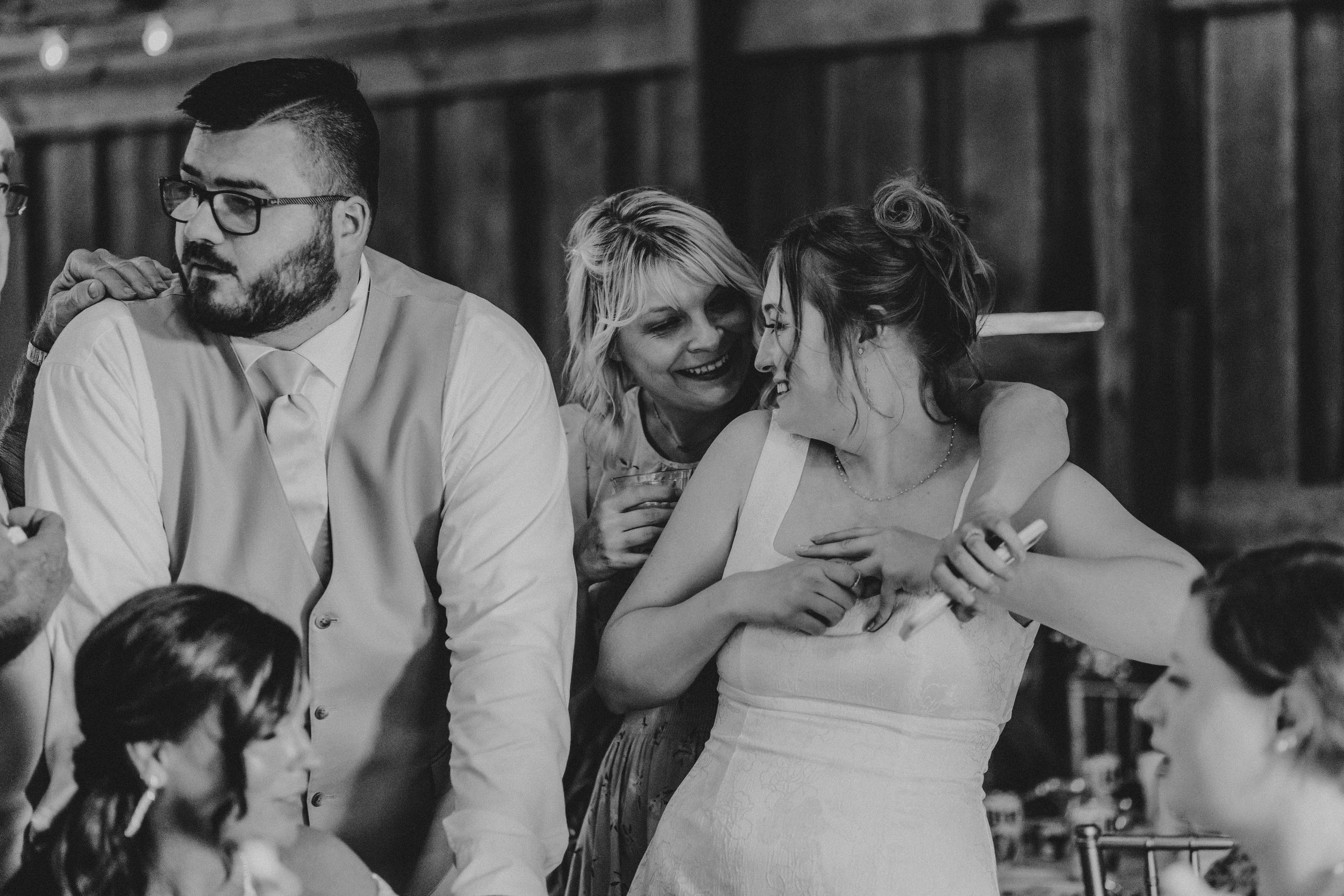 Wedding reception scene with bride and guests laughing together at a table.