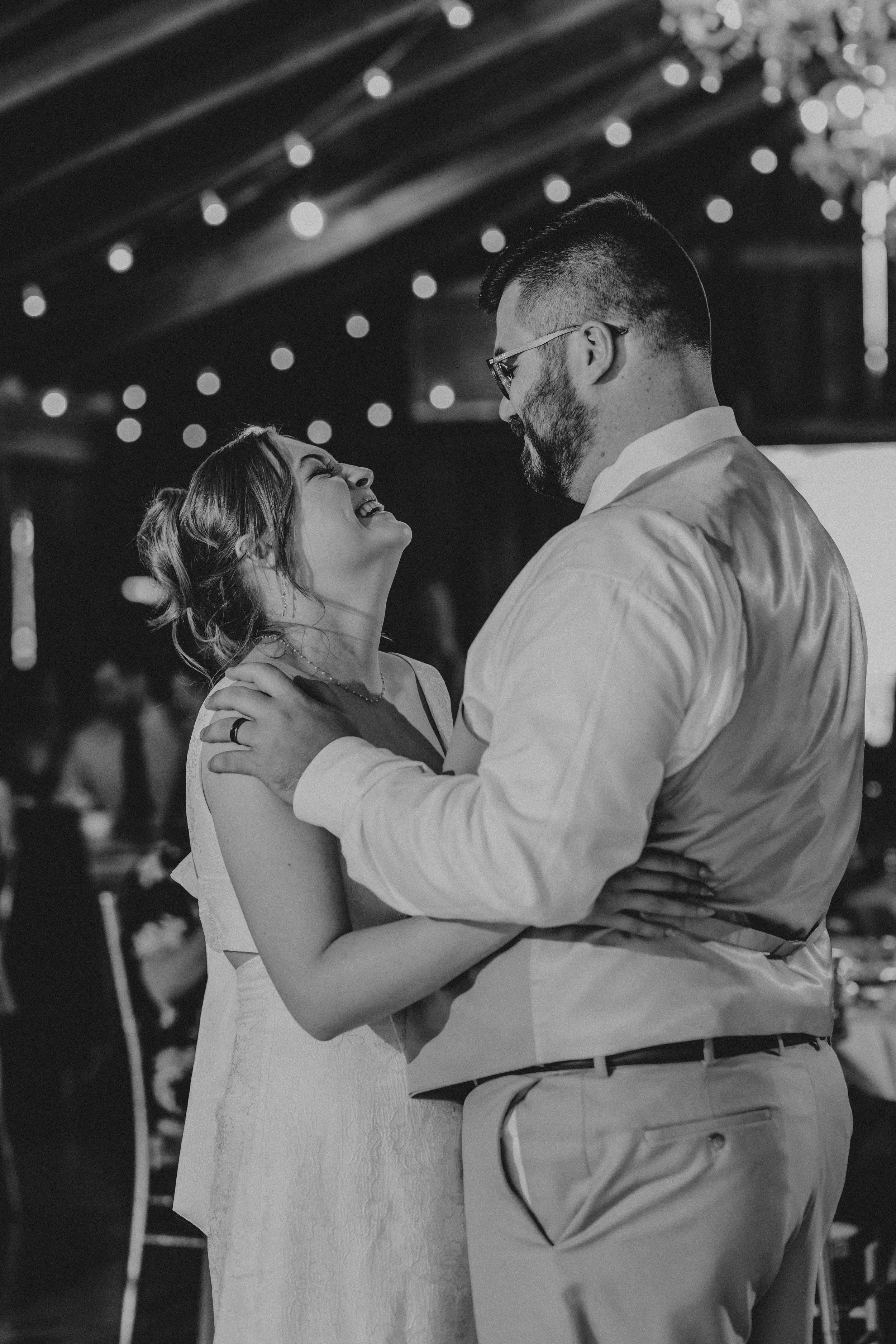 A couple embraces on a dance floor under string lights, creating a romantic wedding reception atmosphere.