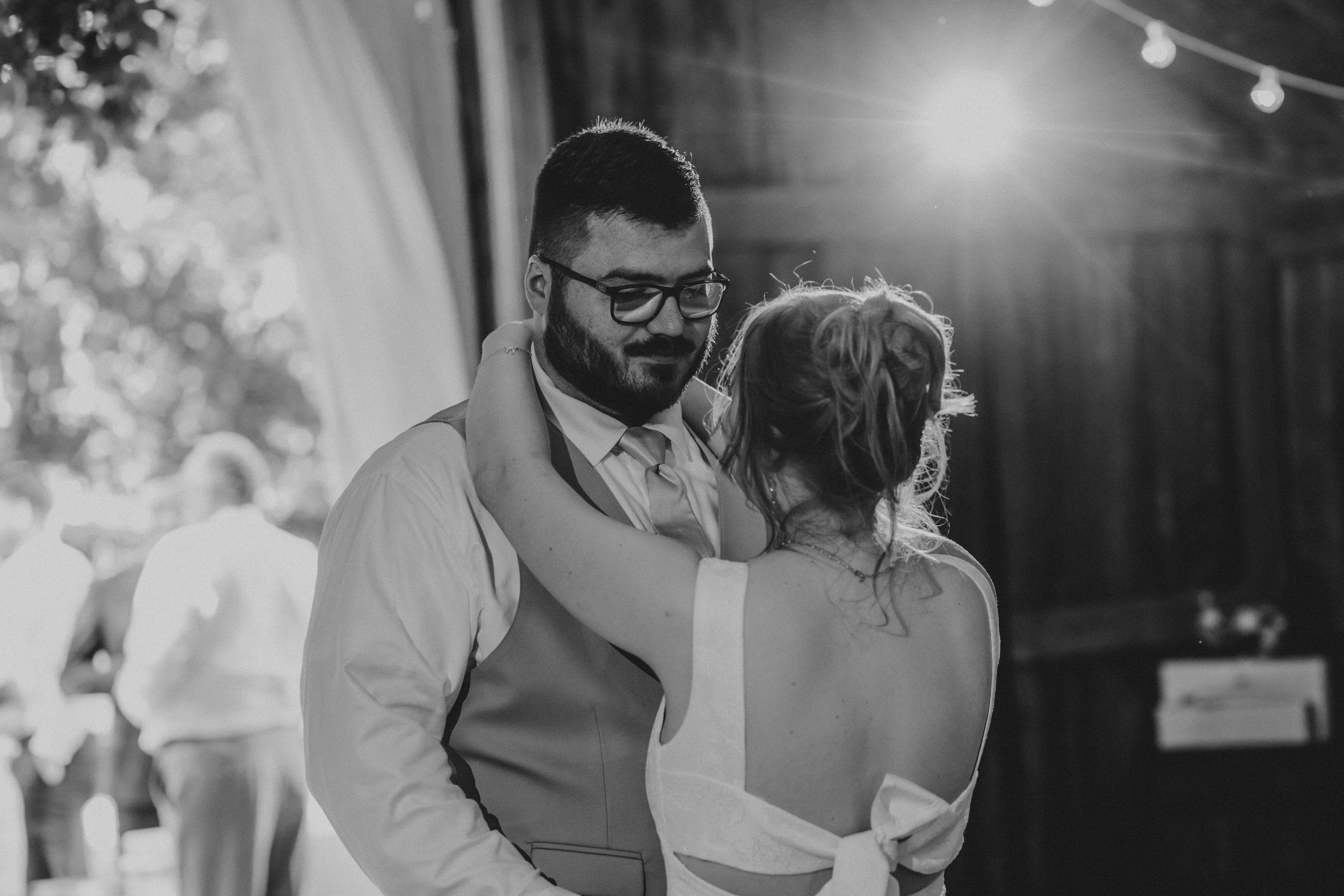 A couple embraces on a dance floor at an outdoor event with string lights in the background.
