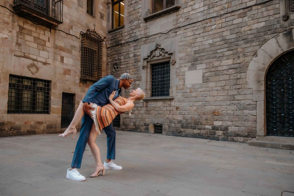 Elegant couple holding hands walking through Barcelona Gothic Quarter morning light.