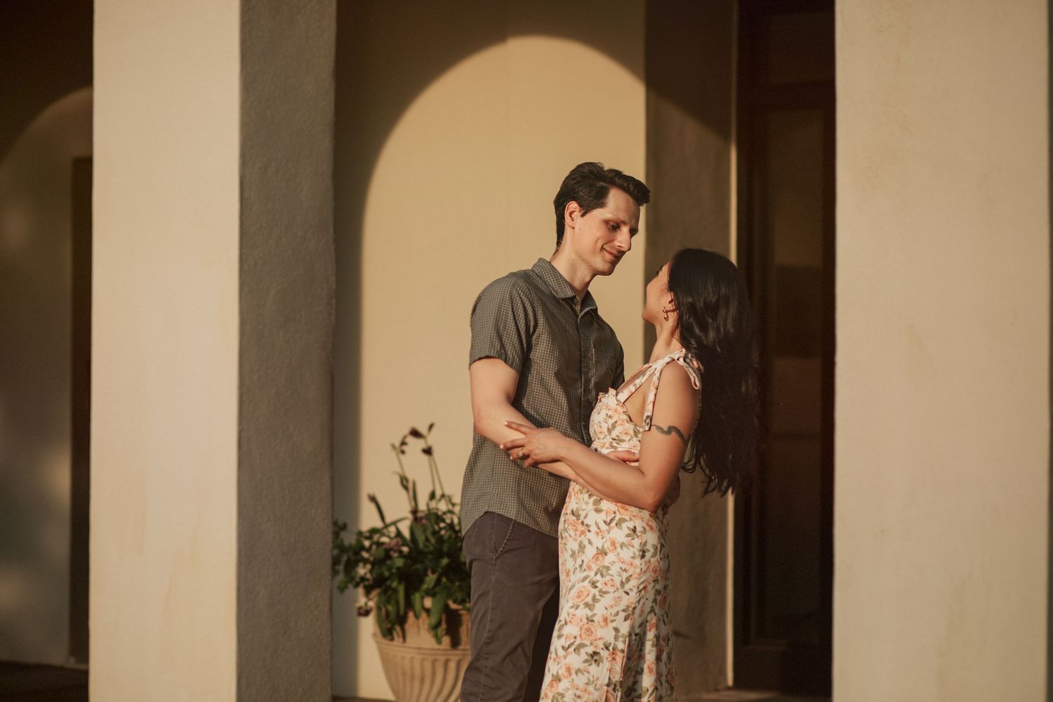 A romantic couple embraces in warm lighting under an arched doorway at sunset at Newfields in Indianapolis.