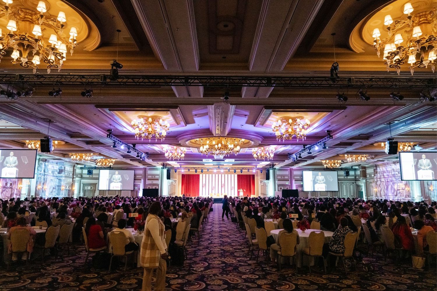 Large elegant ballroom with crystal chandeliers and decorative columns set up for a formal banquet event.
