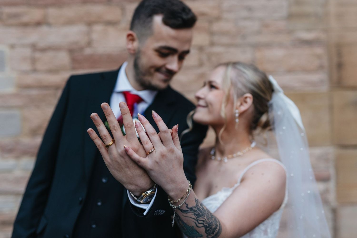 A happy bride and groom share a romantic moment during their wedding photoshoot against a brick wall background.