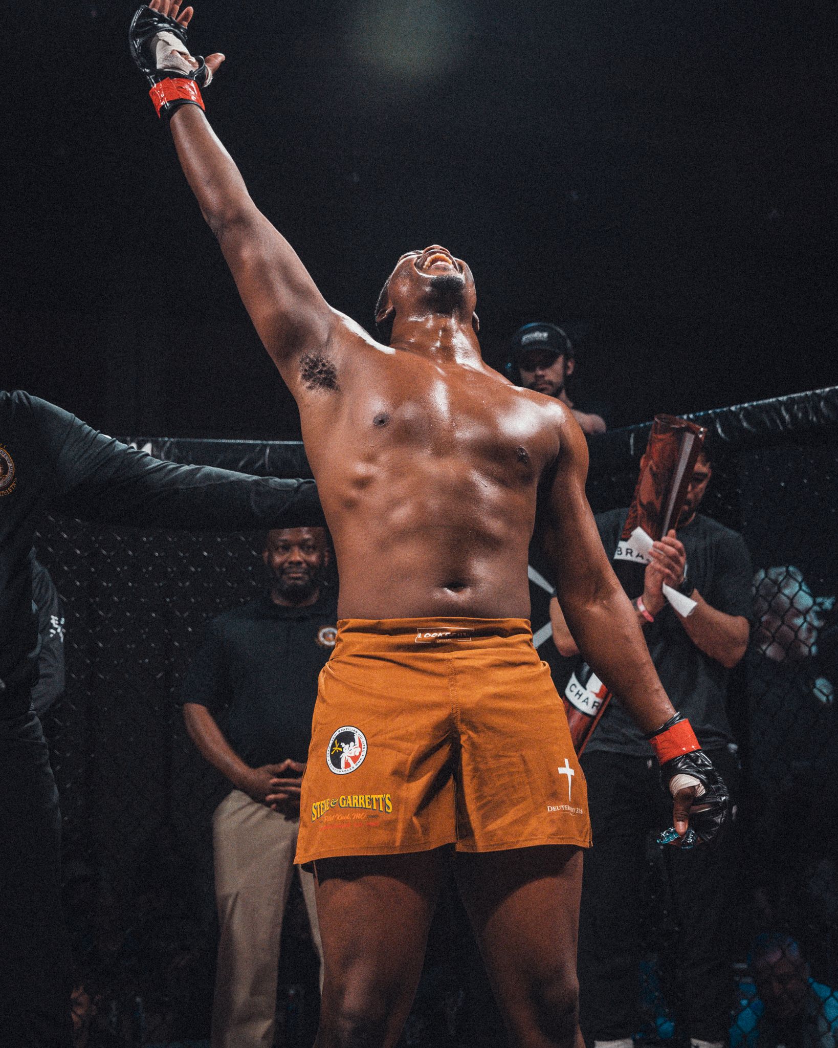 MMA fighter in orange shorts celebrating with arms raised in victory. live event photography st louis.