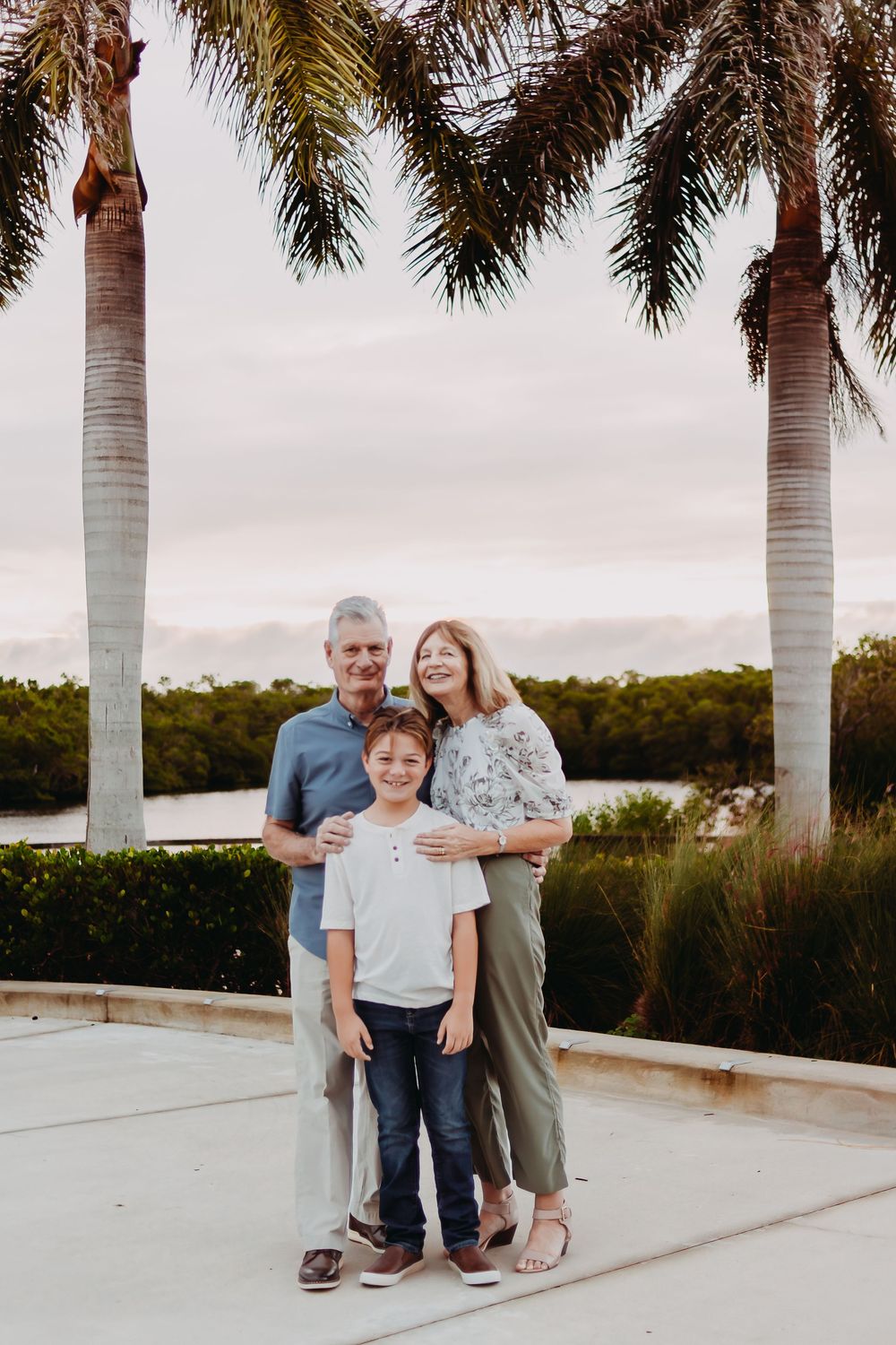 A family poses together on a patio with palm trees and water in the background during sunset.