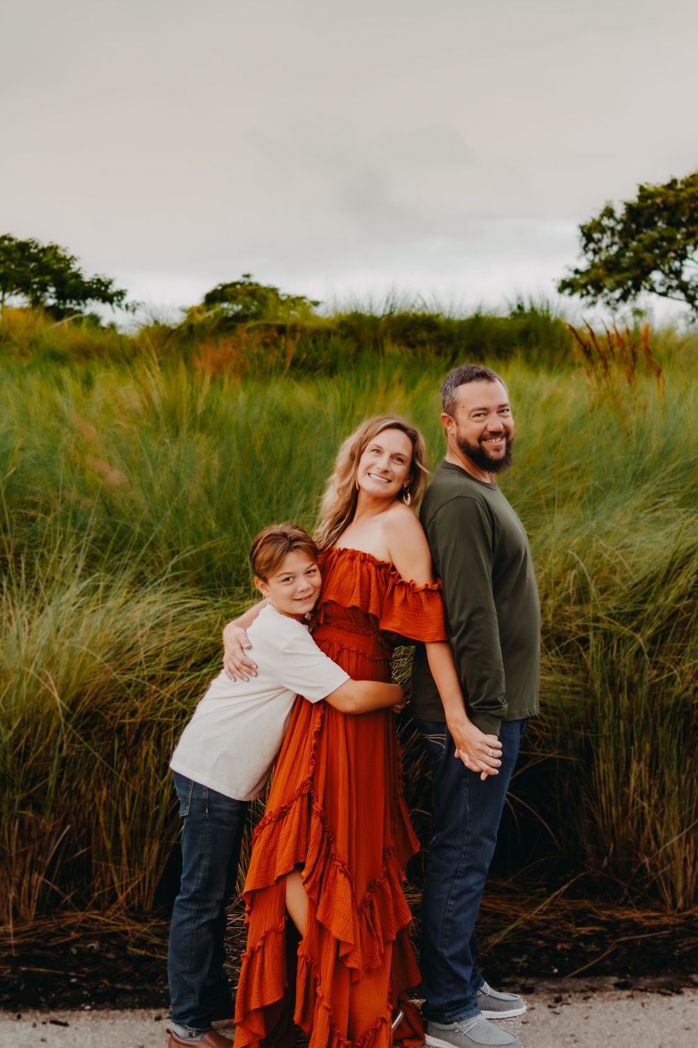 A family stands together in tall grass and natural scenery during golden hour.