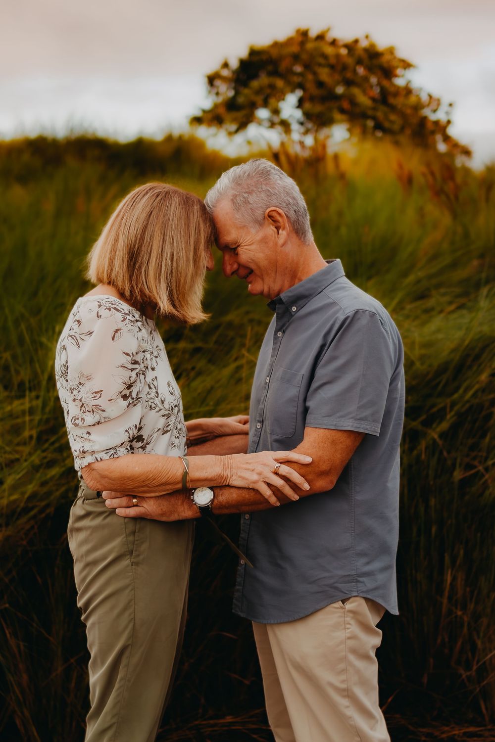 A couple shares an intimate moment in a field during golden hour with a tree silhouetted in the background.