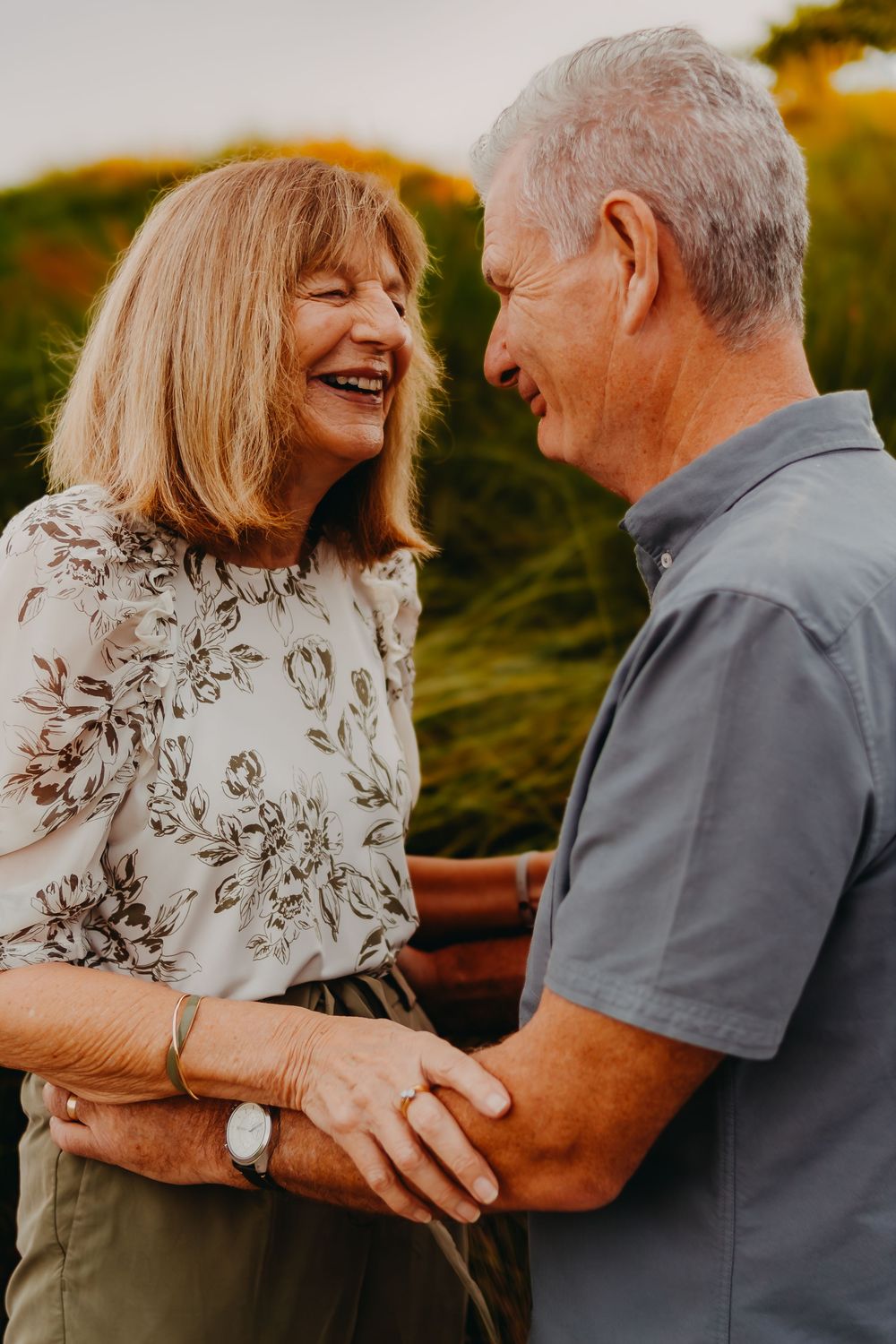 Senior couple laughing and embracing outdoors during golden hour sunset in a romantic moment.