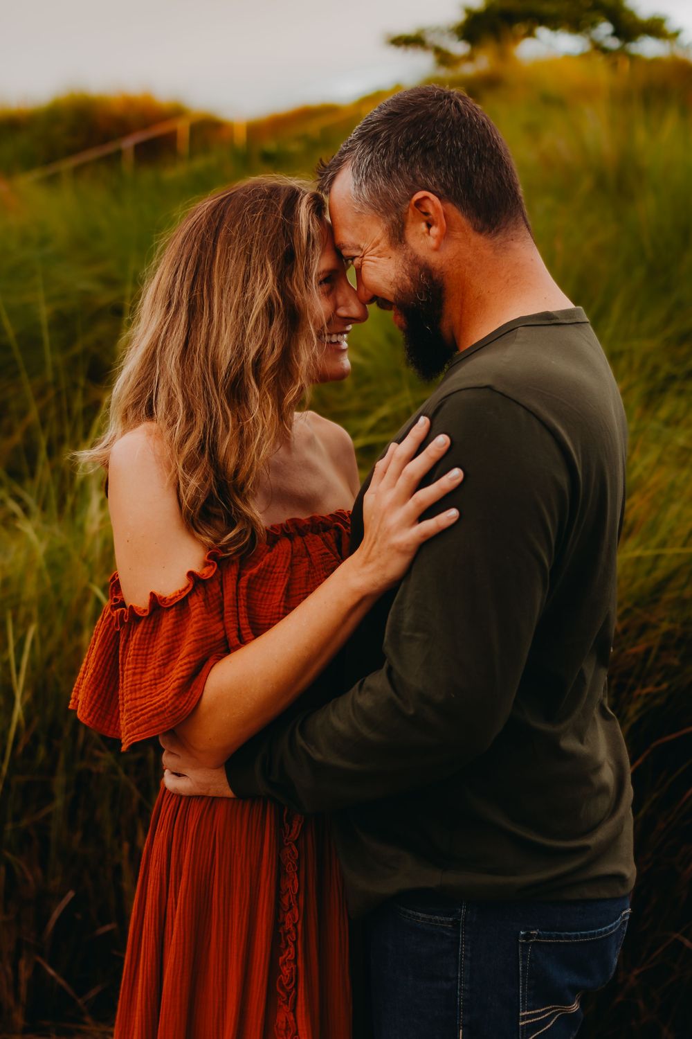 A couple embraces in a golden field during sunset, wearing a red dress and dark shirt as they share intimate moments.