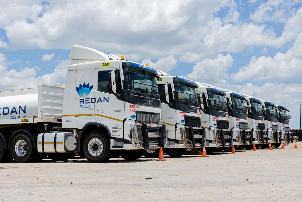 A line of white commercial trucks parked in a row at a distribution center under cloudy skies.