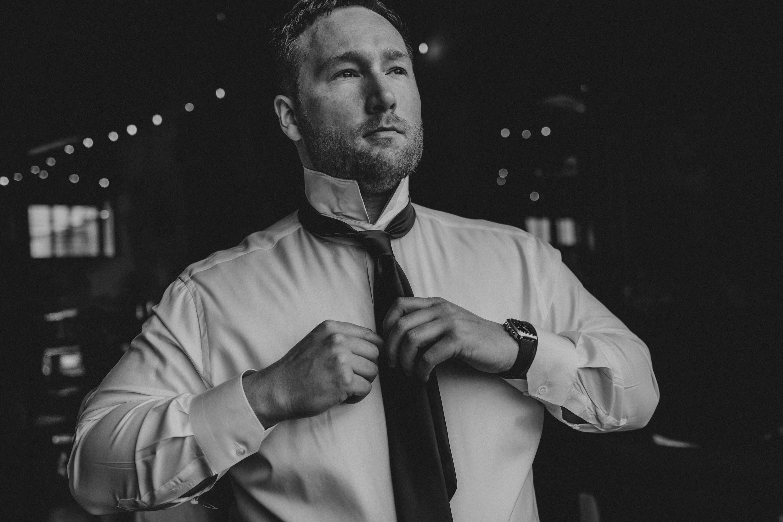 A black and white photo of someone adjusting their tie while wearing a white dress shirt.
