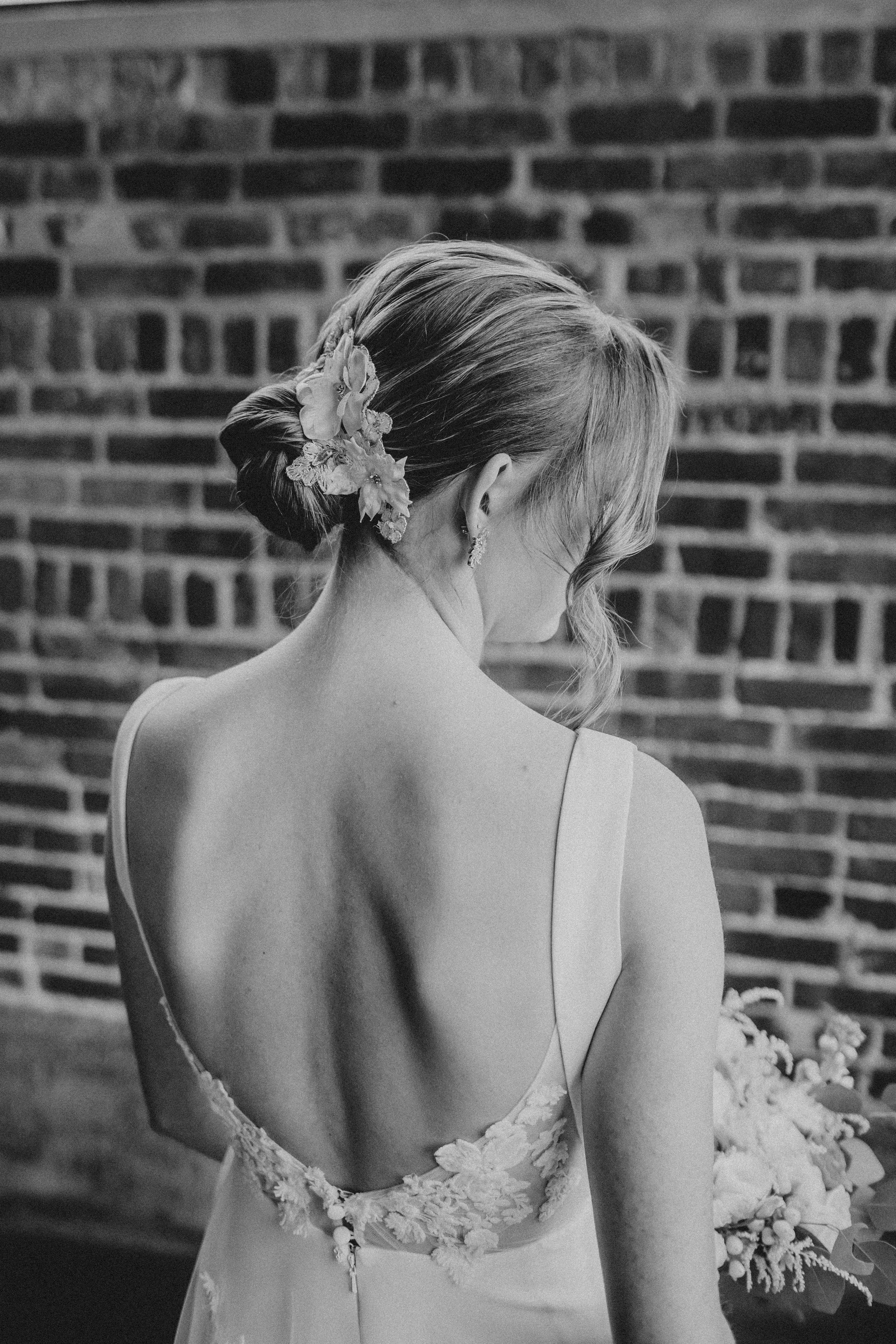 Black and white photo of a bride's back showing delicate lace details on her wedding dress against a brick wall.