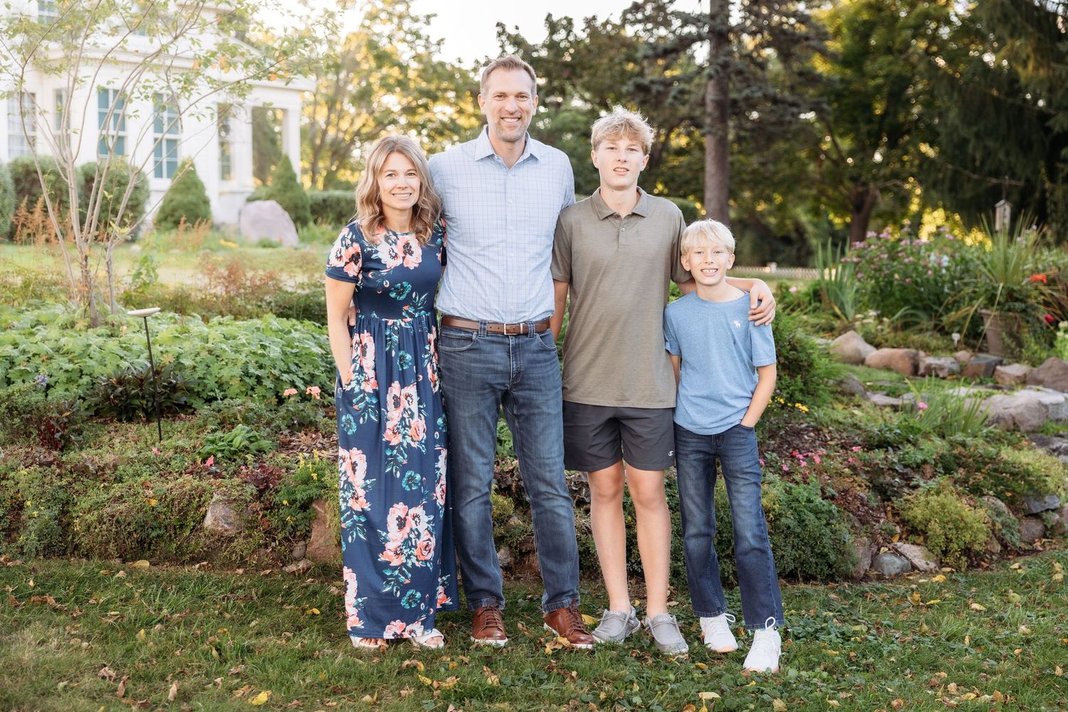 A family poses together outdoors in casual attire on a grassy lawn during a photo session.