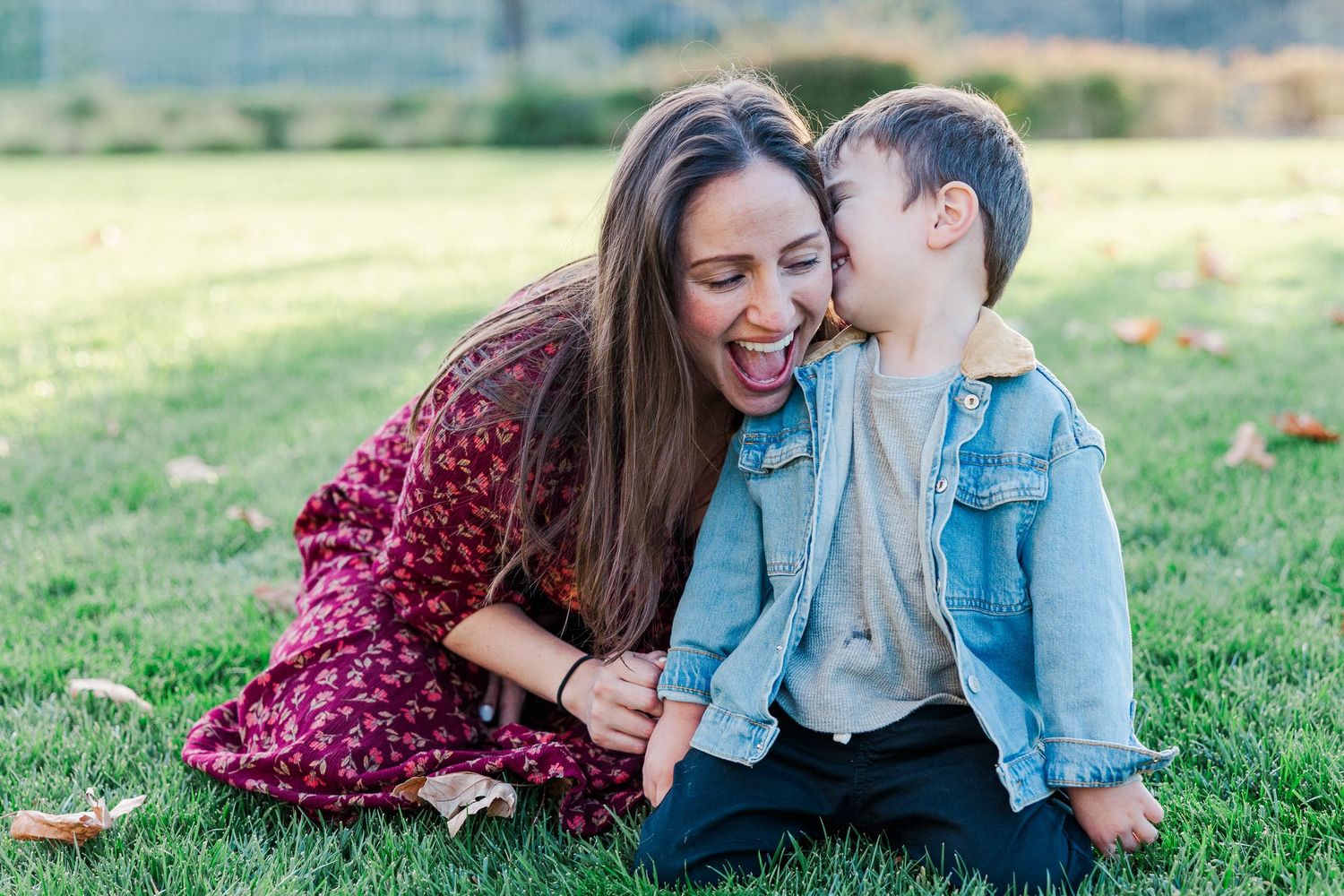 A family wearing burgundy and blue outfits laughs together while laying on grass during an outdoor photo session.