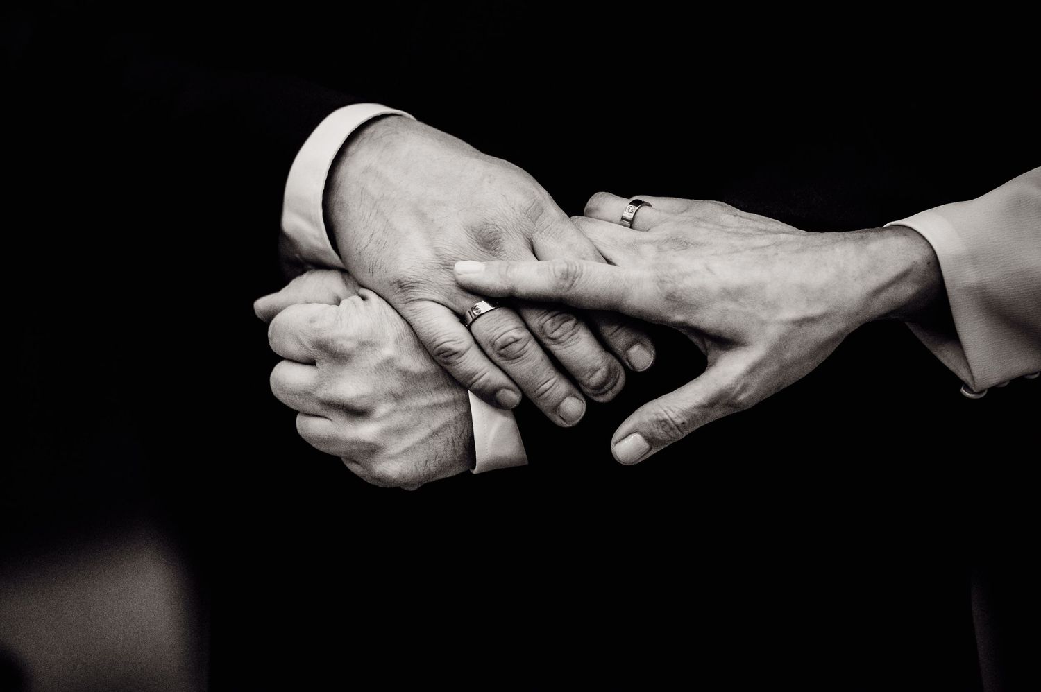 Black and white image of hands reaching towards each other in dramatic lighting against dark background.