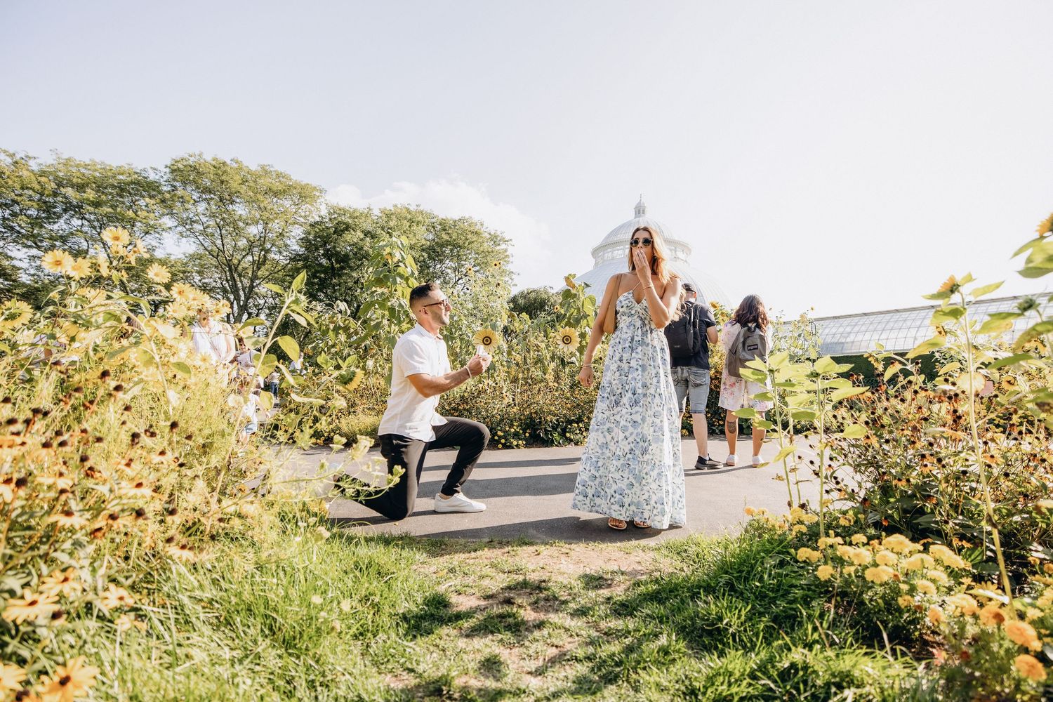People walking along a scenic coastal path with ocean views and yellow wildflowers blooming in the foreground.