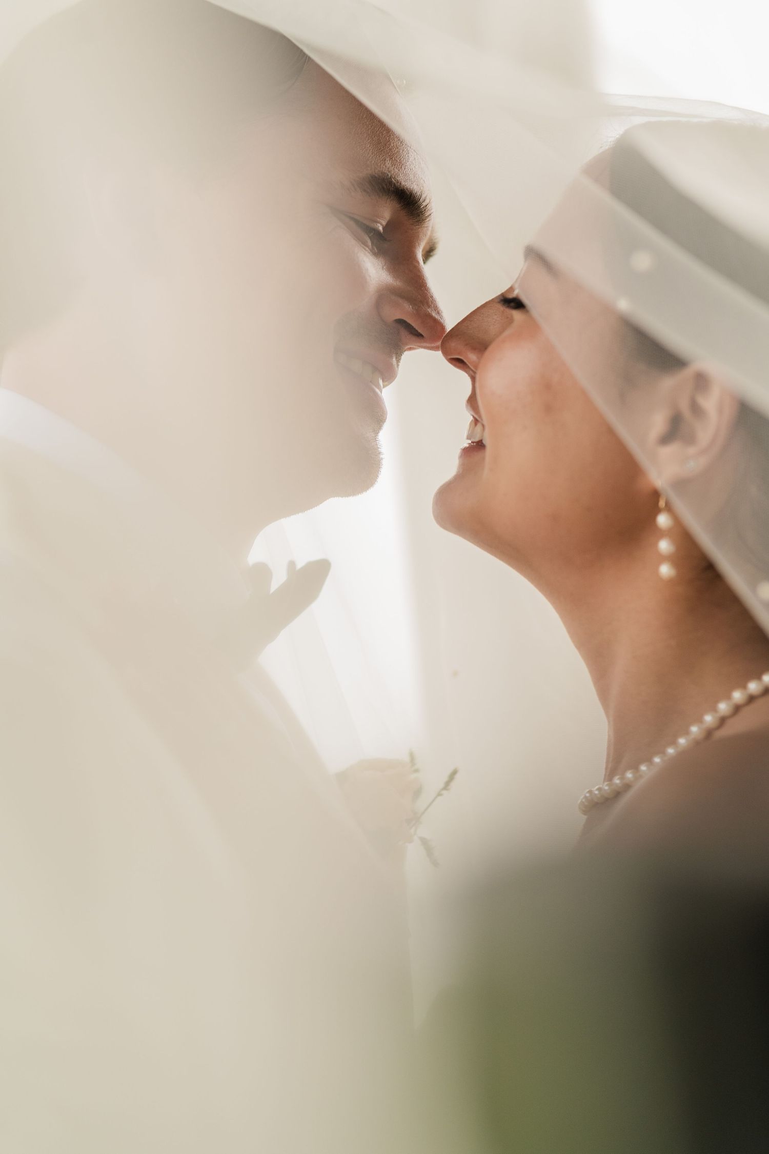 A romantic wedding couple shares an intimate moment in soft lighting with a pearl necklace detail.