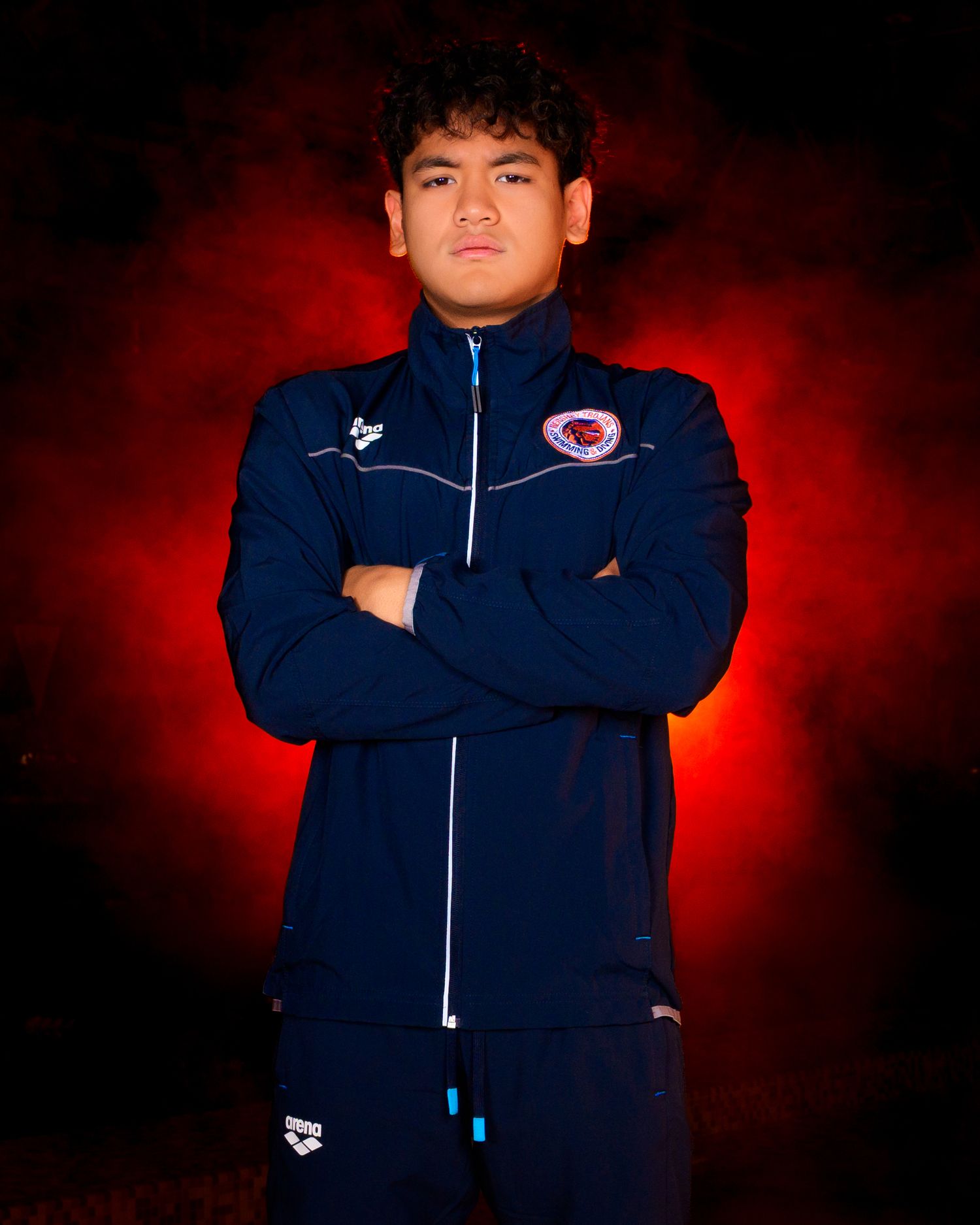 Gavin Tran, Hershey High School Trojan swimmer with blue warmup and orange fog background, by SportsFox Photography, Hershey, PA