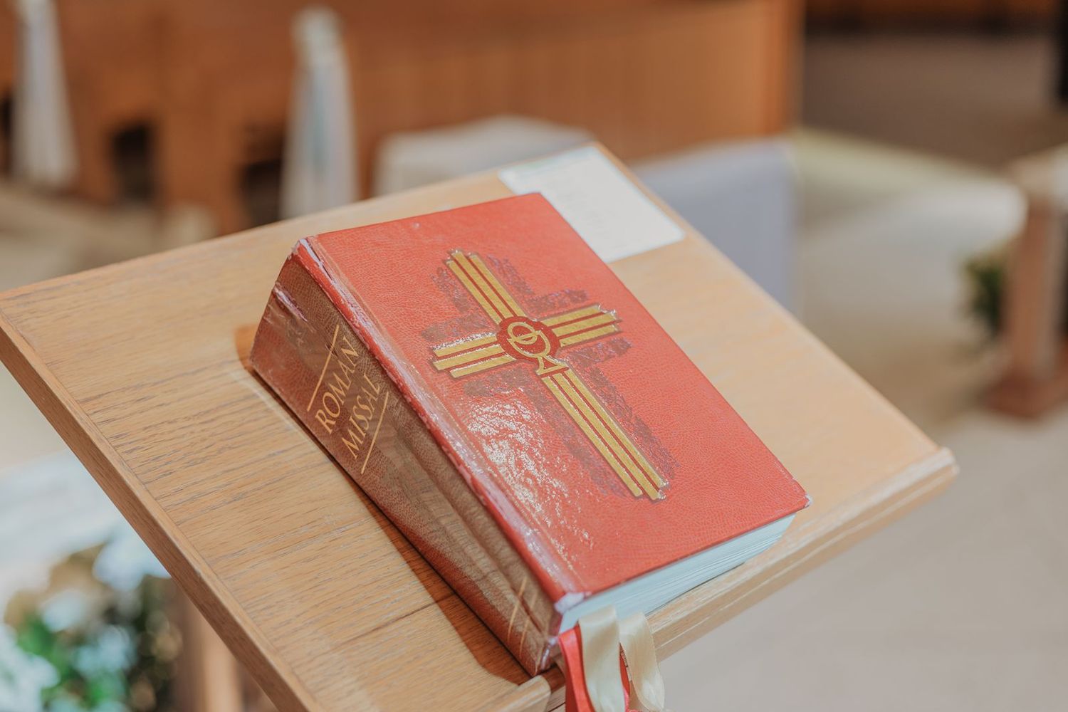 Red Catholic missal book with gold cross on wooden lectern in church ceremony setting.