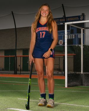 Female athlete in Hershey field hockey uniform on turf field, holding stick, team photo day by SportsFox Photography.
